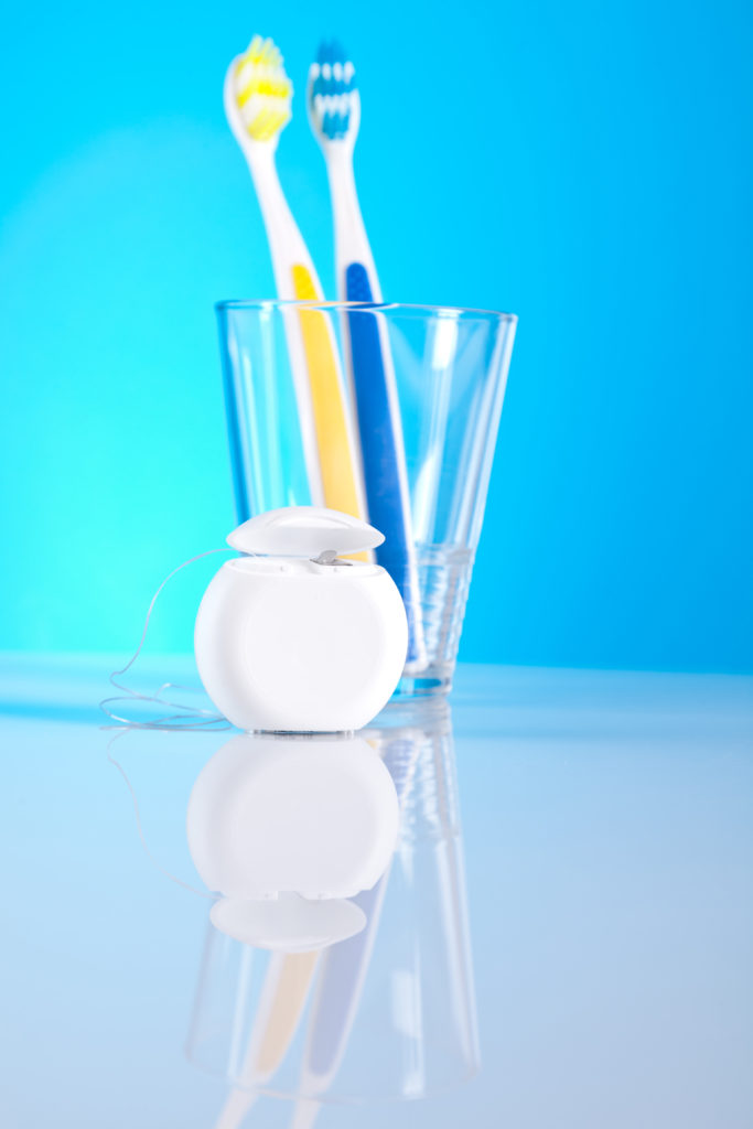 two toothbrushes in a cup and some dental floss