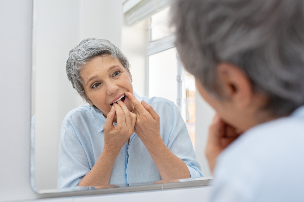 older woman cleaning her teeth with dental floss